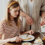 A mother assists her daughter during a cozy breakfast at home.