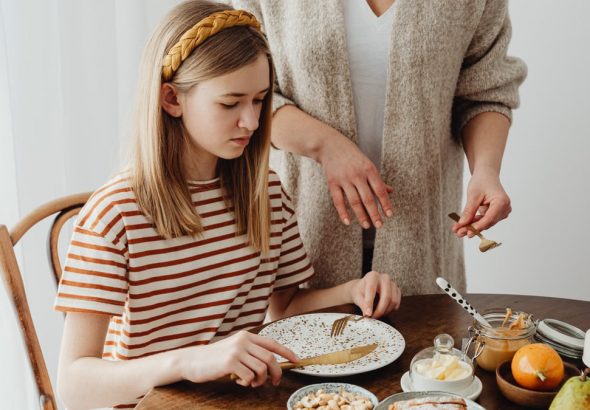 A mother assists her daughter during a cozy breakfast at home.