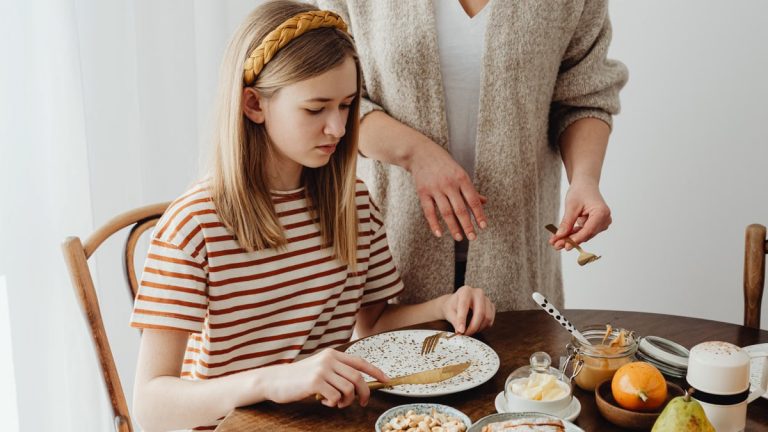 A mother assists her daughter during a cozy breakfast at home.