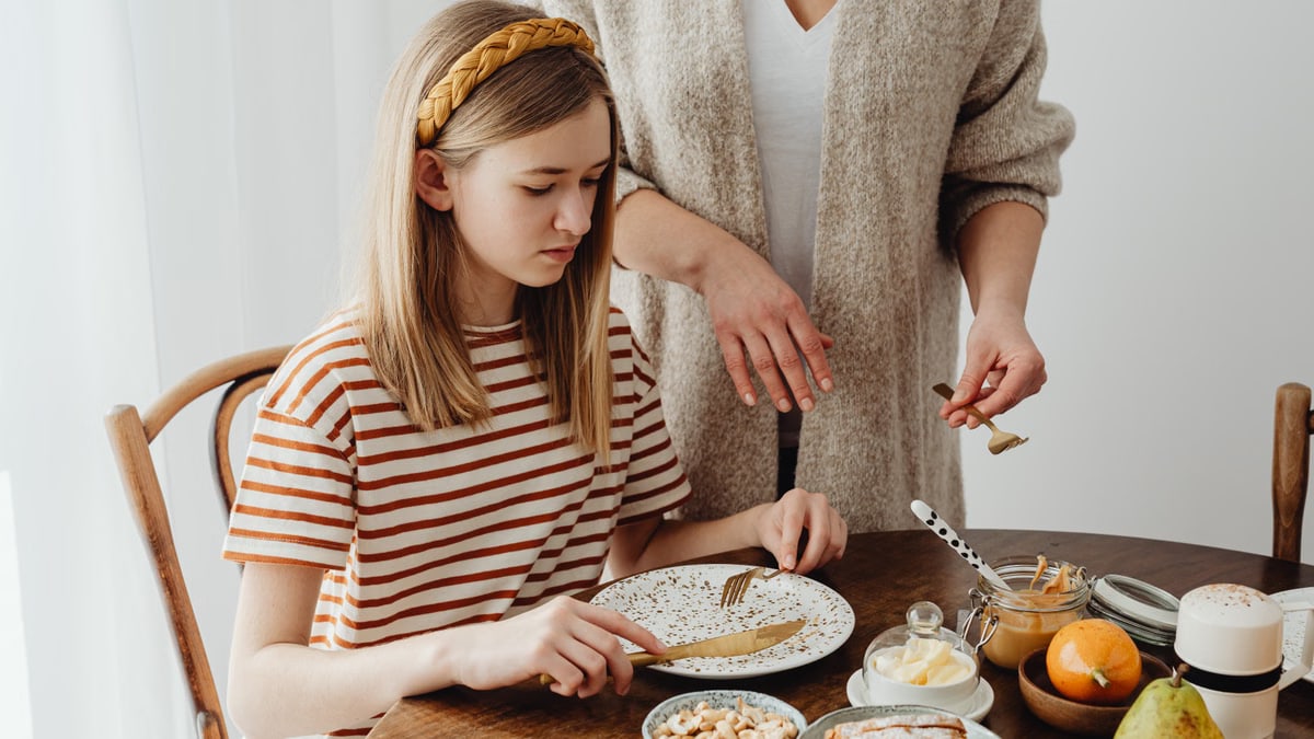 A mother assists her daughter during a cozy breakfast at home.